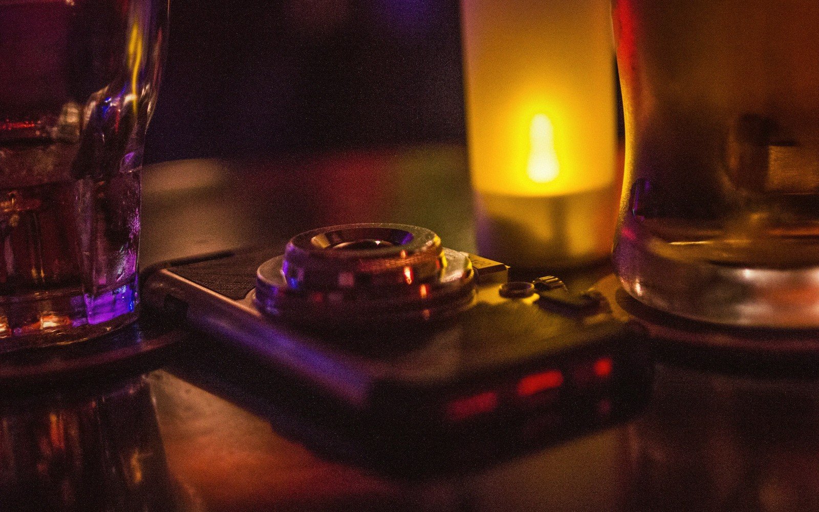 Camera with a round lens resting on a bar table beside drinks and a candle