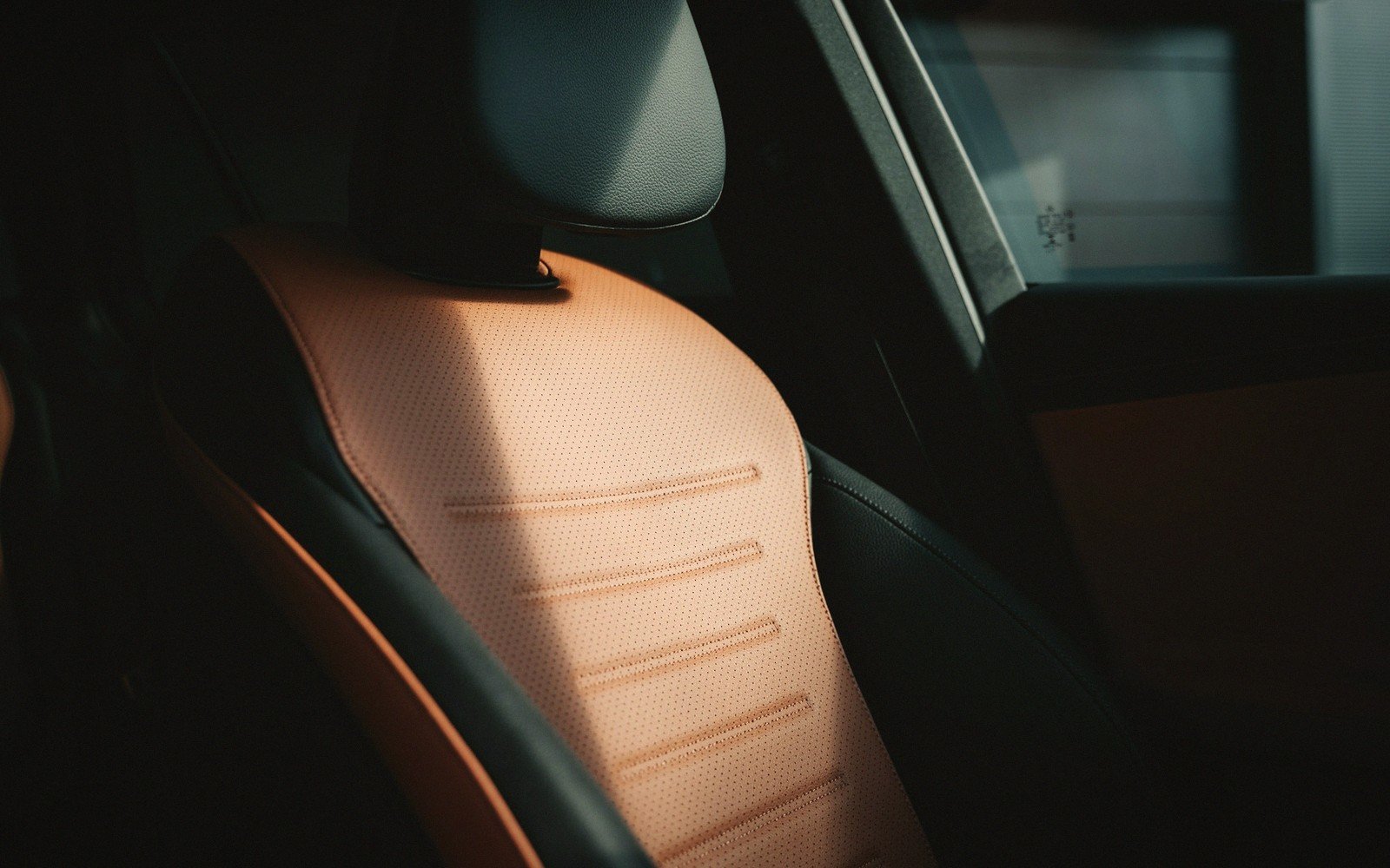 Sunlight strikes a car's tan leather seat with black perforated trim and headrest