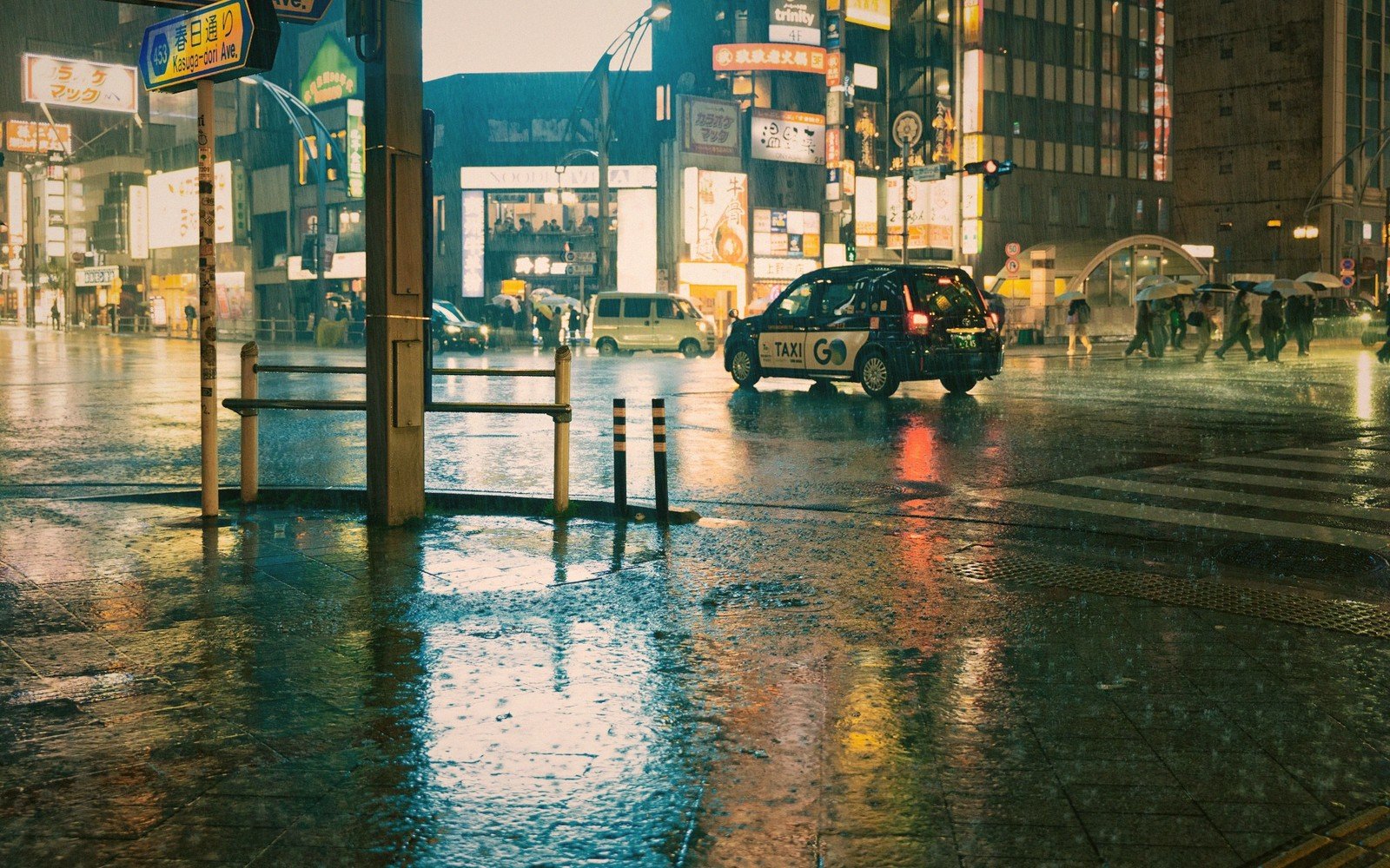 A taxi crosses a rain-soaked intersection under illuminated signs at night