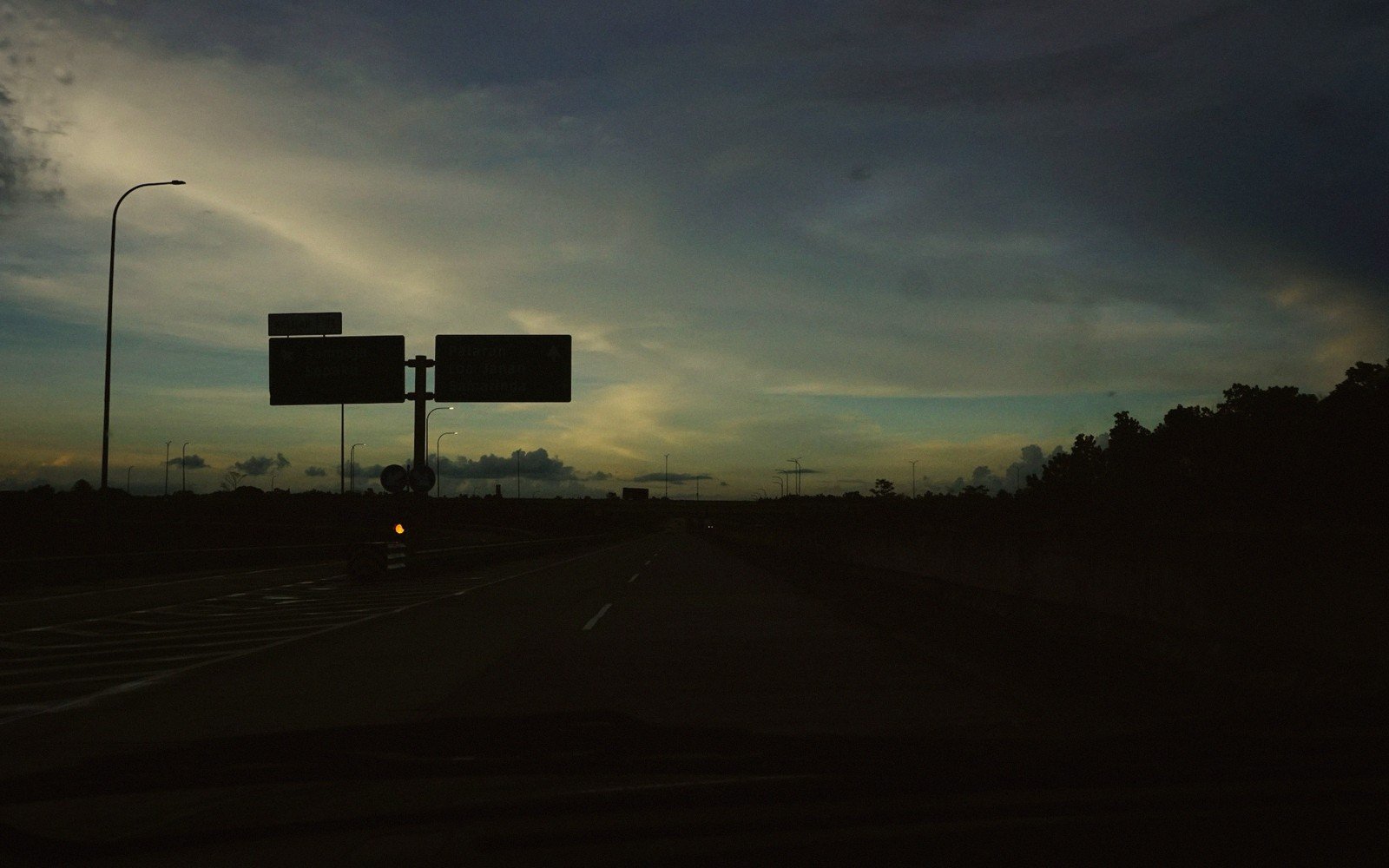 Highway overhead signs silhouetted against a dusky sky with streaked clouds
